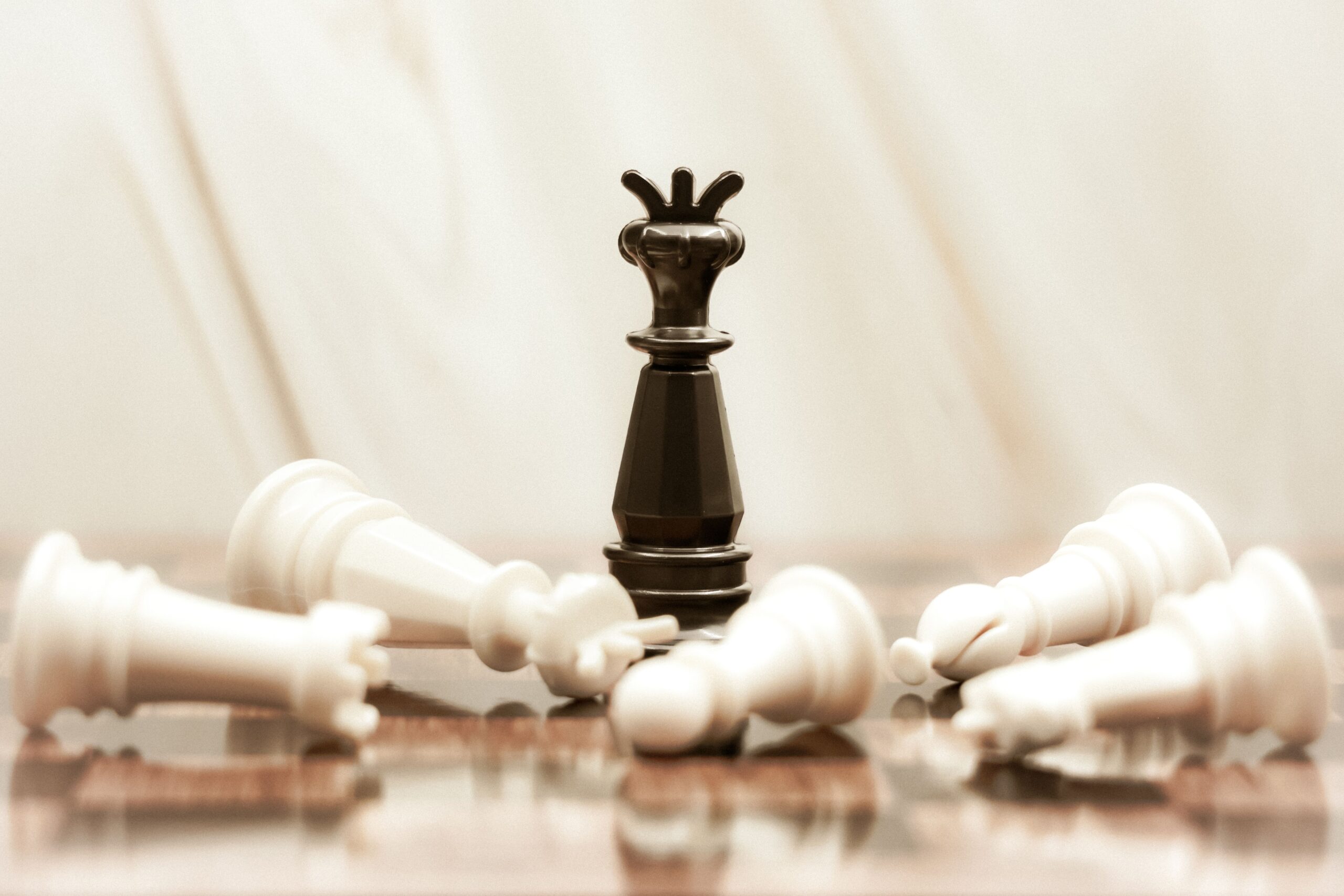 A black chess queen stands triumphant among toppled white pieces on a reflective surface.