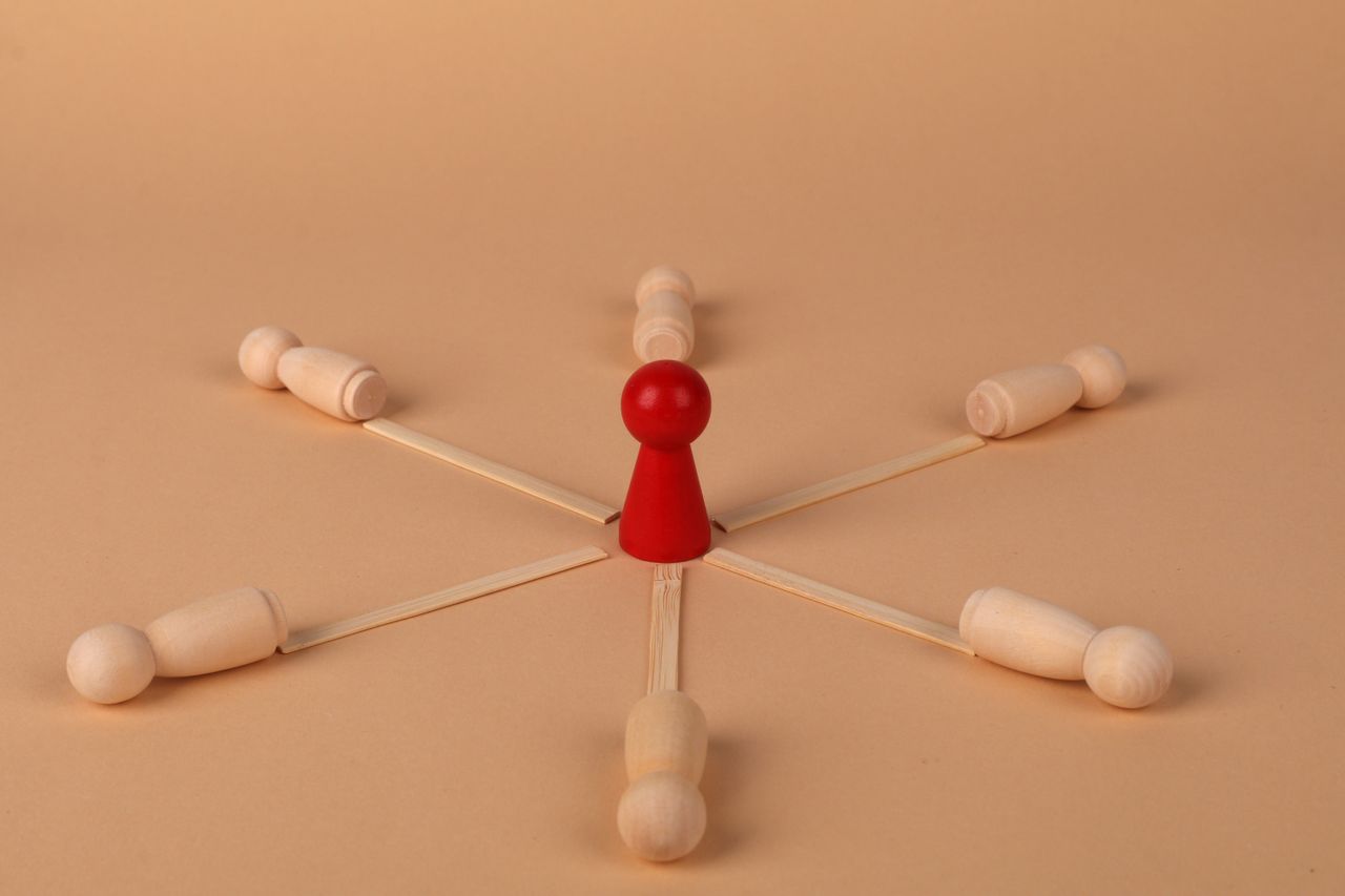 Red leader figure connected to wooden figures, emphasizing leadership and teamwork.
